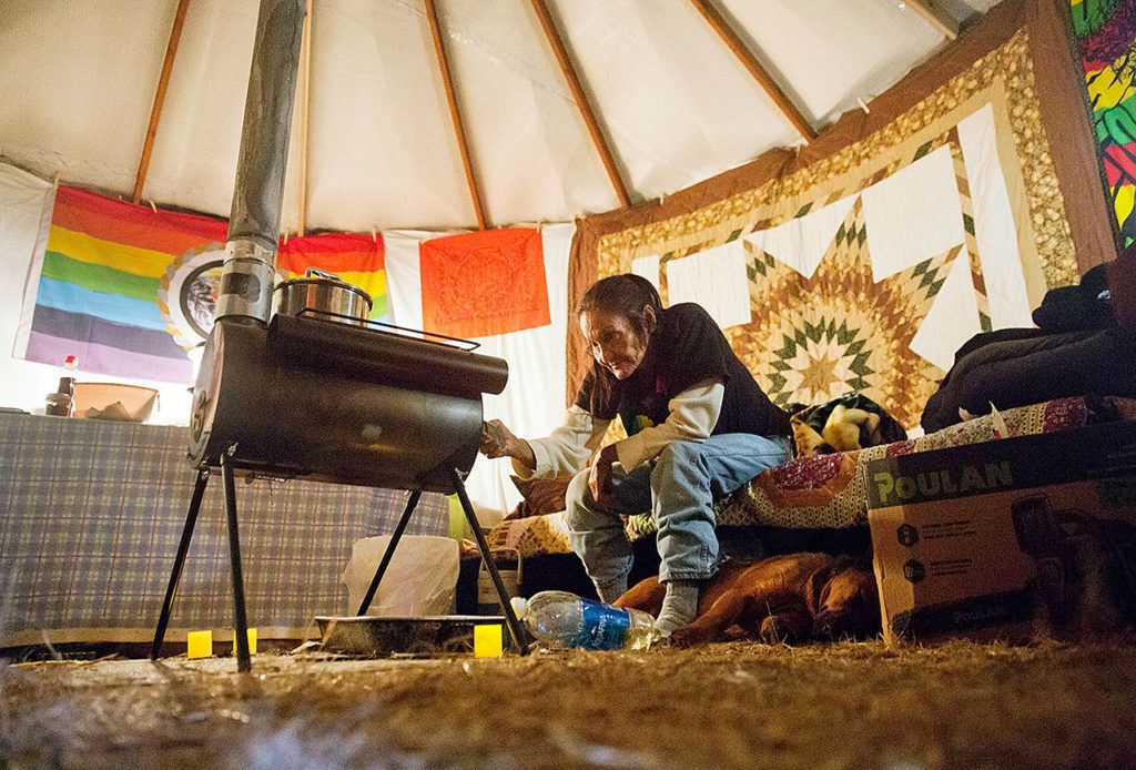 In this Tuesday, Nov. 29 photo, Grandma Redfeather of the Sioux Native American tribe sits by the wood stove in her yurt at the Oceti Sakowin camp where people have gathered to protest the Dakota Access oil pipeline in Cannon Ball, North Dakota. “I’m sitting here in my prayer” said Redfeather of living at the camp since July. “I’ll stand on my treaty and fight.” (AP Photo/David Goldman)
