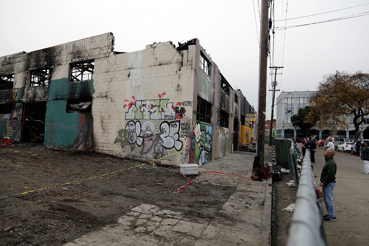People look at the scene of a warehouse fire from behind a fence on Tuesday in Oakland , California. The fire killed dozens of people during a electronic dance party as it raced through the building, in the deadliest structure fire in the U.S. in more than a decade. (AP Photo/Marcio Jose Sanchez)