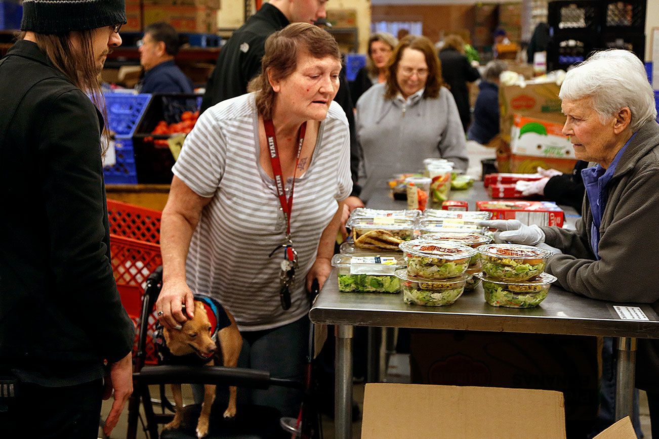 Assisted by volunteers, Adam Szydel (left) and Marge Beauchamp (right), Kerrin Thompson, of Marysville, picks out a few items at the Marysville Food Bank, just days before Thanksgiving. Thompson was also able to get something for her small service dog, Diego. (Dan Bates / The Herald)