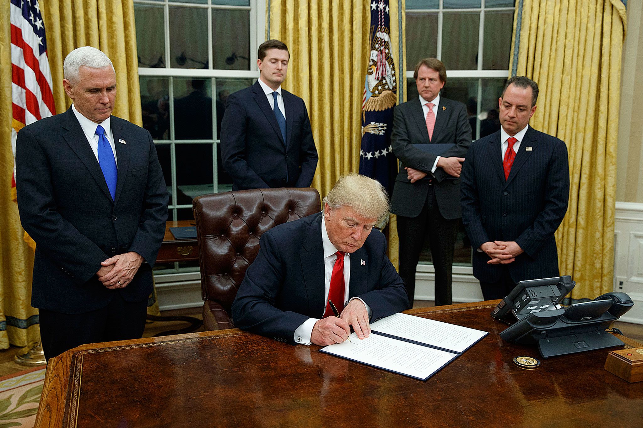 President Donald Trump, flanked by Vice President Mike Pence and Chief of Staff Reince Priebus, signs his first executive order on health care Friday in the Oval Office. (AP Photo/Evan Vucci)