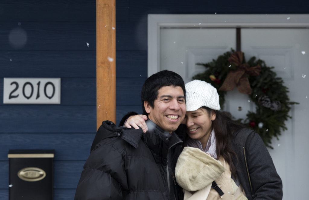 Ray and Sandy Flores hug on their front porch after accepting the keys, earlier that morning, to their new home from Habitat for Humanity of Snohomish County on Saturday, Dec. 17, 2016 in Everett. The Flores and their three young kids became the new owners of Phoenix II, a house in North Everett, which they contributed over 500 hours of sweat equity in its construction. (Andy Bronson / The Herald)
