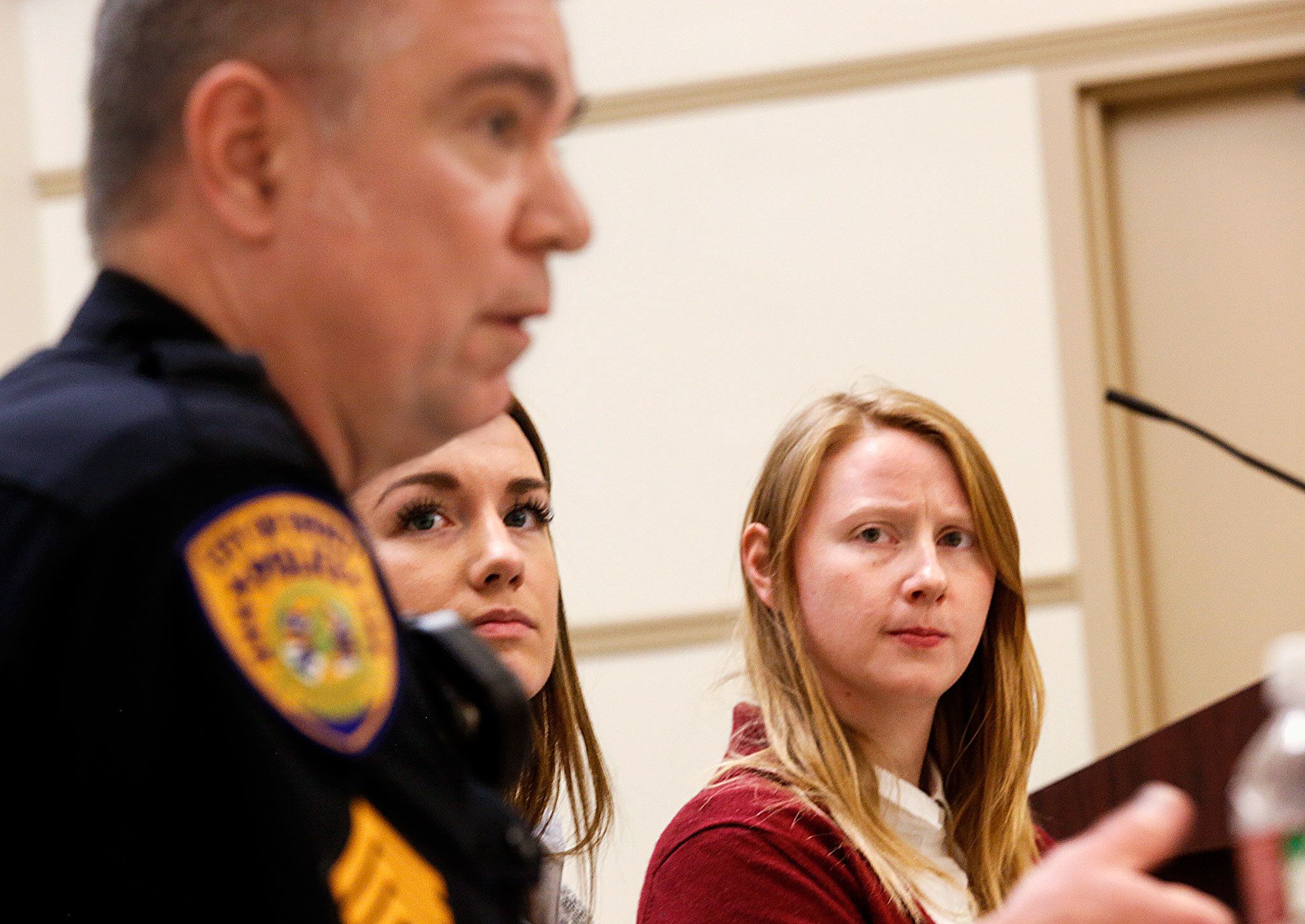 Staci McCole (right) and Kaitlyn Dowd, social workers embedded with the Everett Police Department, watch Everett Police Sgt. Mike Braley as he responds to a question from the audience Tuesday night at the Everett Public Library. (Dan Bates / The Herald)