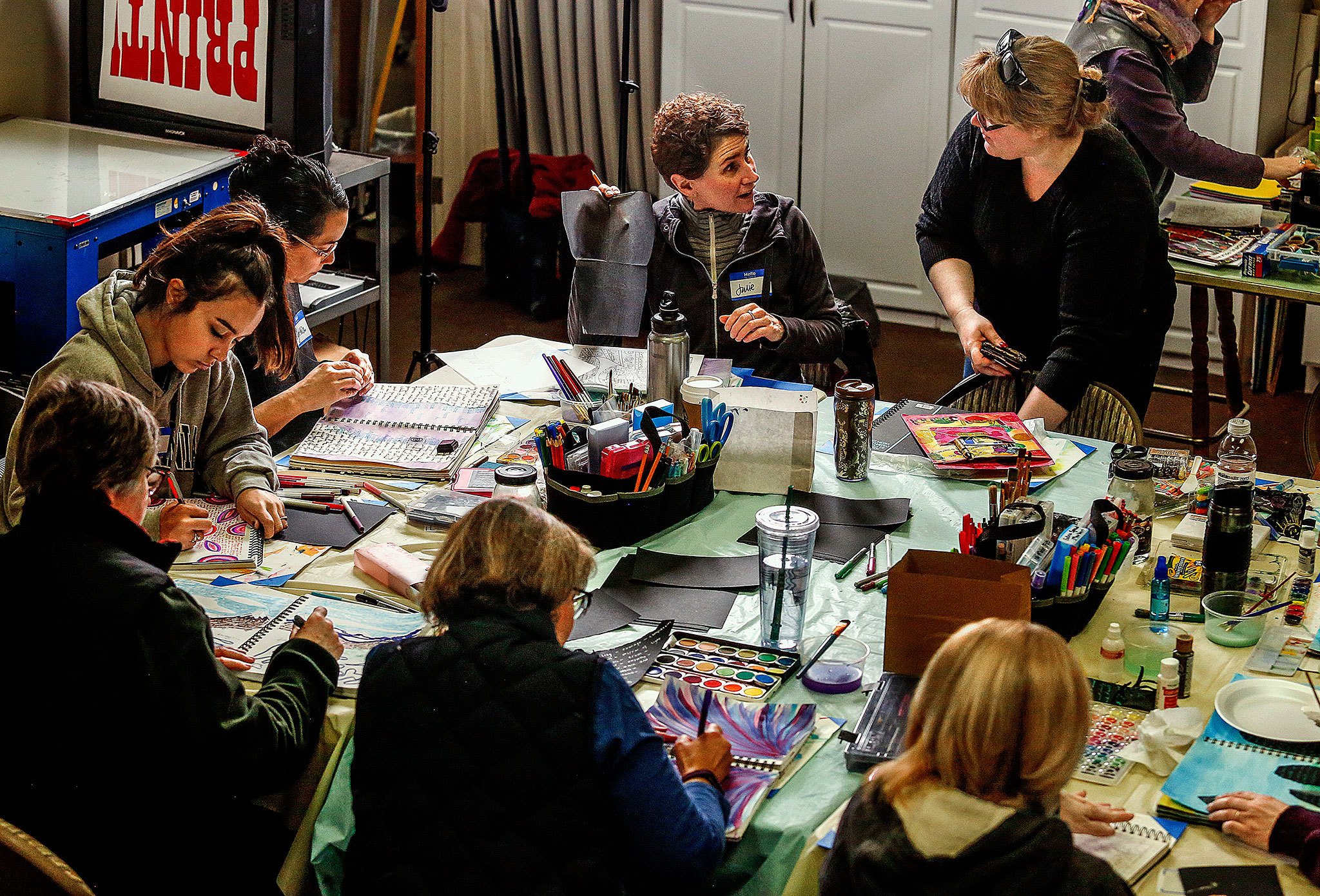 At a table filled with art supplies, Christin Eubanks (standing) and Julie Selmo exchange greetings and ideas. (Dan Bates / The Herald)
