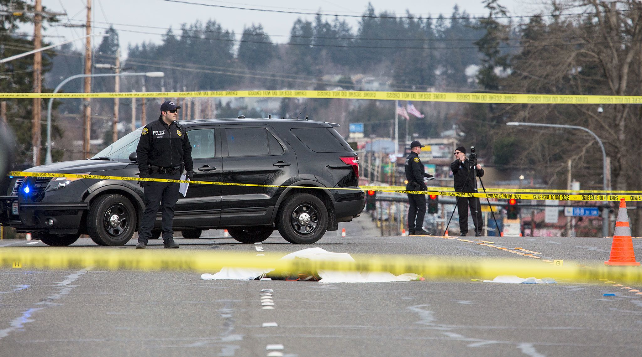 A detective (right) takes photos at the scene where a Lynnwood police officer fatally shot a man in the 19200 block of Highway 99 on Monday. (Andy Bronson / The Herald)