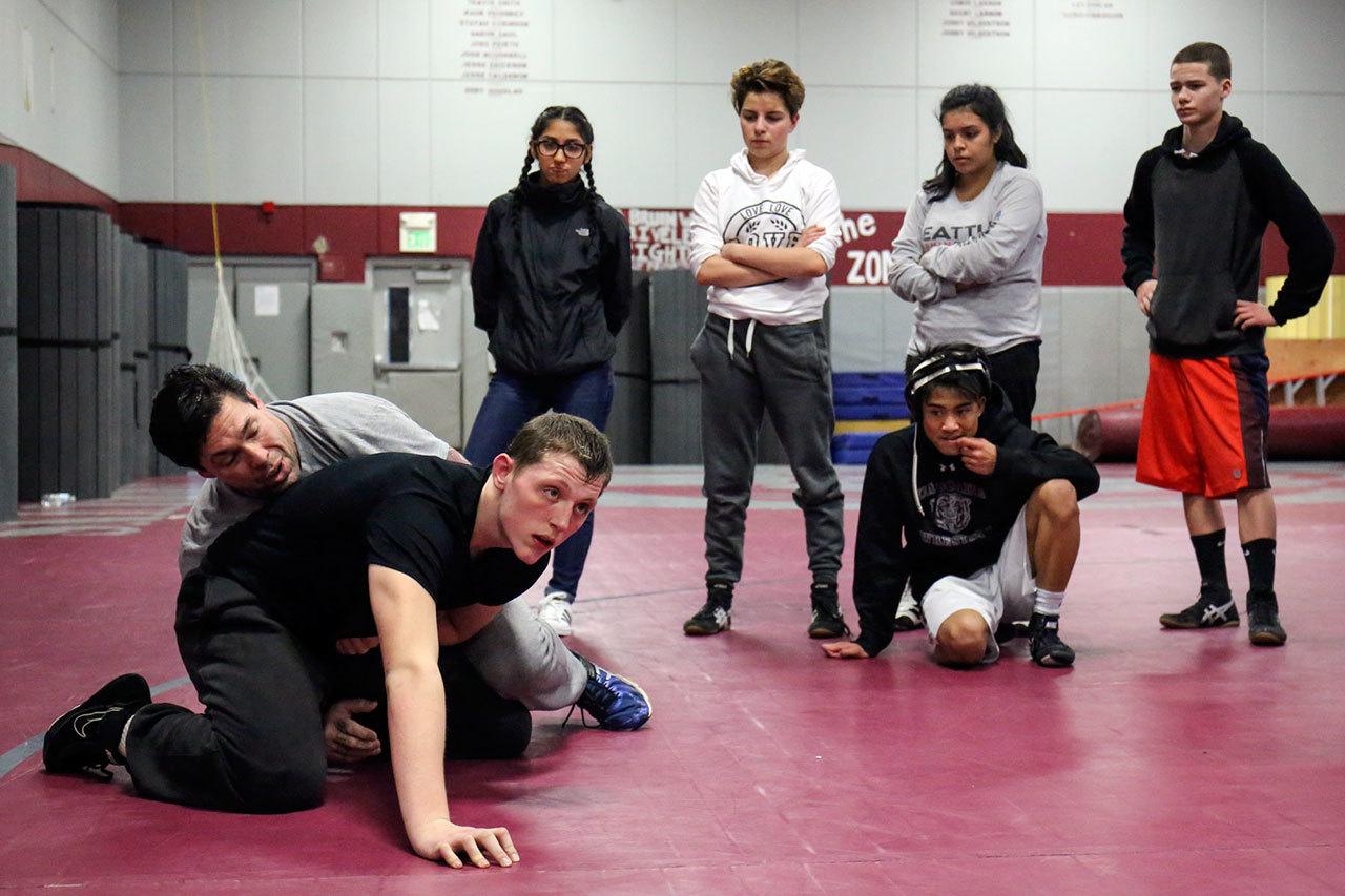 Cascade wrestling coach Brooklyn Obregon (far left) demonstrates a technique on Adam Holston during practice on Jan. 18 in Everett. After the death of his father, Jery, in June of 2016, Holston moved in with Obregon and his wife, Cindy. (Kevin Clark / The Herald)