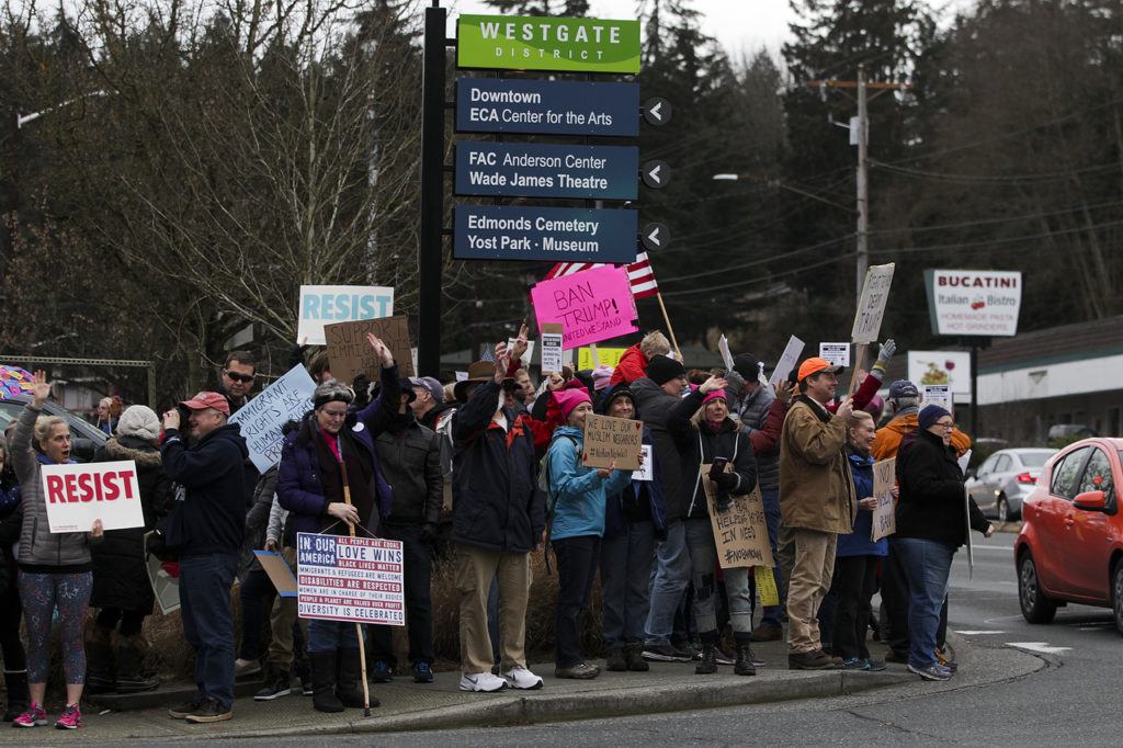 Protesters wave signs and cheer during a gathering at the corner of 100th Avenue West and Edmonds Way in Edmonds on Sunday, Jan. 29. The protest aimed to raise awareness and voice opposition to President Trump’s executive order banning immigrants from seven Muslim-majority countries from entering the U.S. The executive order, signed on Friday, triggered massive protests at airports across the country as details came out about refugees and other visitors being detained despite having all documents necessary for entry into the U.S. (Ian Terry / The Herald)
