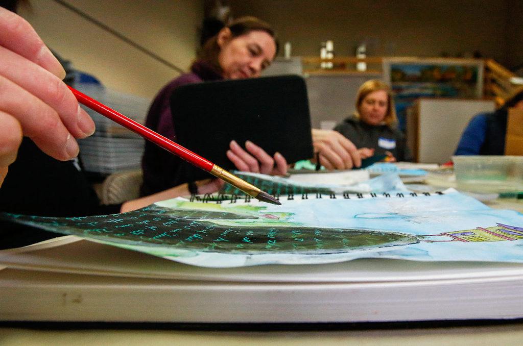 Class leader Karen Dawn works with a red paintbrush on her own journal (foreground) while Susan Curtis (middle) and Dawn Everett (back) concentrate on theirs. (Dan Bates / The Herald)
