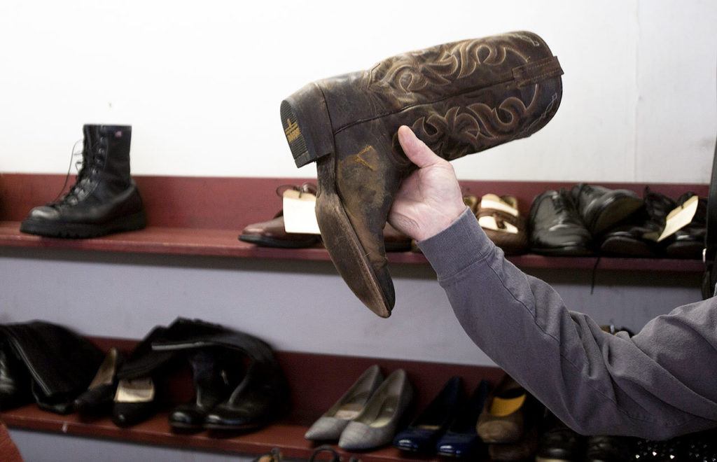 A customer shows off a boot with a ‘V’ shaped tear in it as he drops it off for repair at the People’s Shoe Repair in Everett. (Andy Bronson / The Herald)
