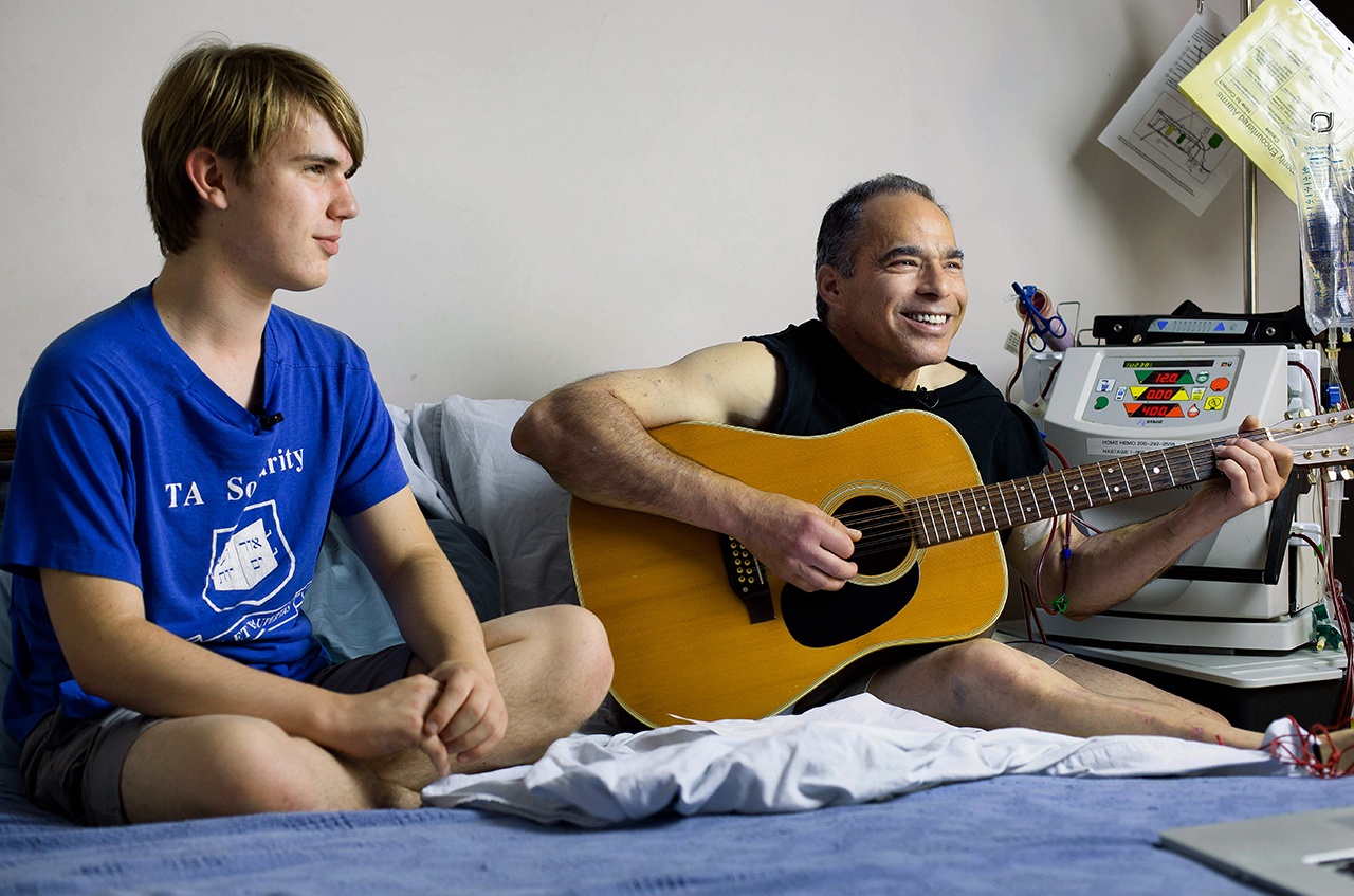 Michael Goldberg plays guitar while spending time with son Asher de Forest during one of Goldberg’s at-home dialysis sessions in 2014. Goldberg, an associate professor at the University of Washington Bothell, passed away Dec. 26. (Photo by Quinn Russell Brown)