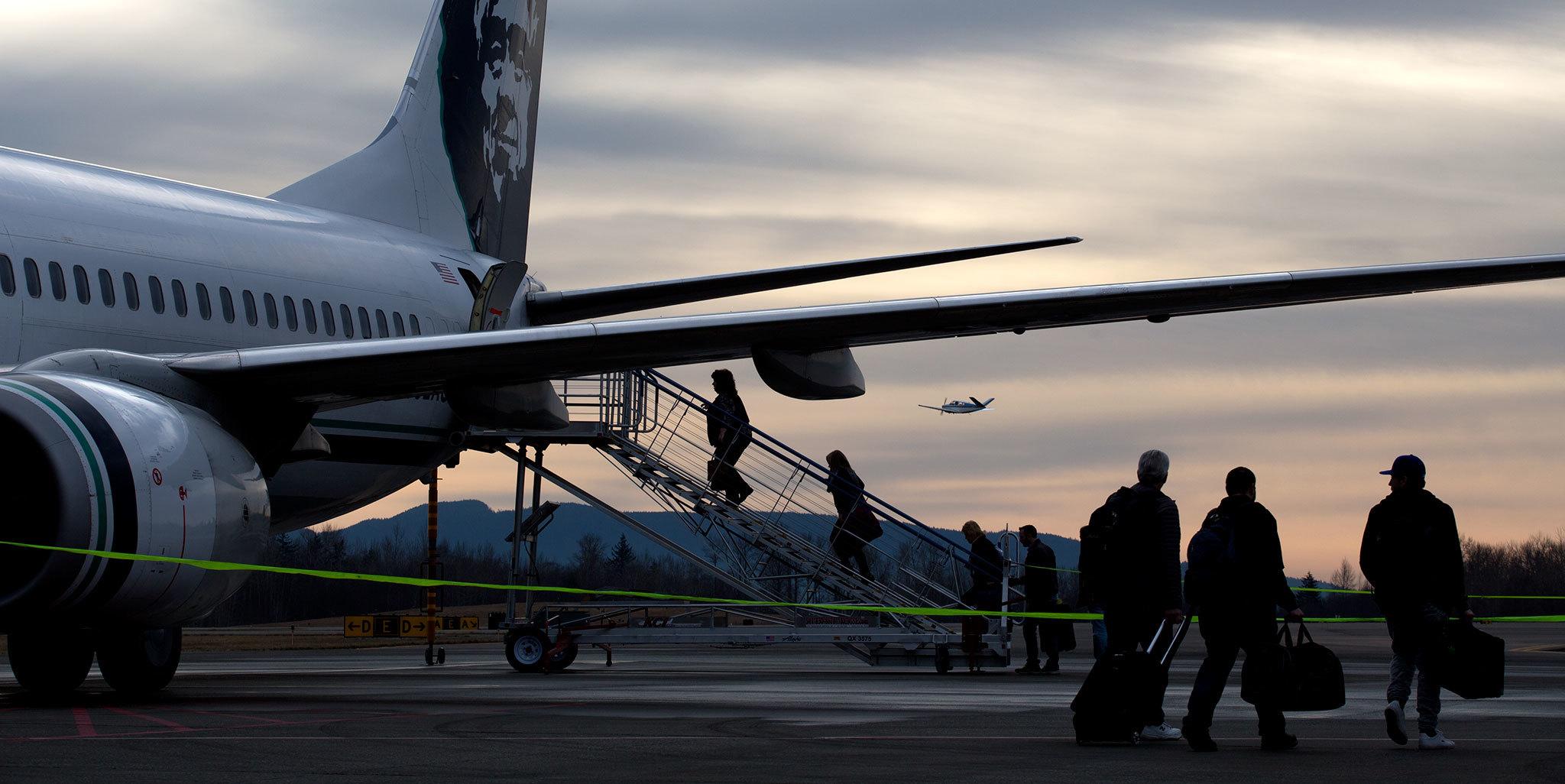 As a private plane passes by, passengers board to the rear of jet at Bellingham International Airport on Thursday, Jan. 26, in Bellingham. Alaska Airlines flies yearound to Seattle and Portland; and seasonally to Kona and Maui, Hawaii, starting in November. Kona flights end April 1 and Maui flights end April 2. (Andy Bronson / The Herald)
