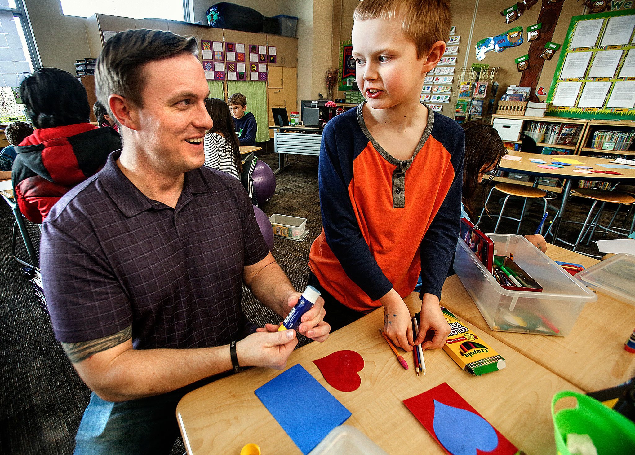 Fourth-grader Kasen Cooley explains the ins and outs of making Valentine’s Day cards to Navy veteran Benjamin Studley on Thursday, beginning with gluing on the heart and ending with what to write on it. “We have a list of ideas on the wall over there,” said the polite 10-year-old, “if you need help thinking of something to say.” (Dan Bates / The Herald)