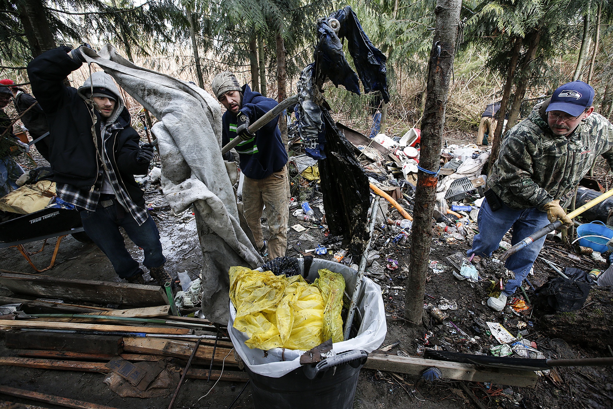 Volunteers (from left) Sean Holman, of Wenatchee, Shawn Quiacusan, of Renton, and Curtis Rodgers, of Lake Stevens, pile heaps of garbage into a container during a cleanup of homeless encampments along the Skykomish River near Monroe on Saturday. The cleanup was organized by RiverJunky, a group founded in late 2016 that cleans up trash along waterways. (Ian Terry / The Herald)