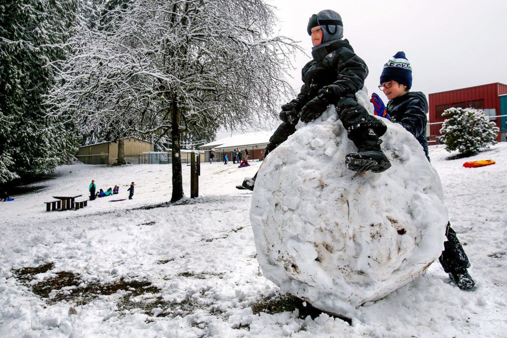 At the popular park outside Mount Pilchuck Elementary School in Lake Stevens, where they would normally be in class, kindergarten student James Eichert, 6, sits atop a huge snowball while first-grader Mason Jones, 7, packs more snow around him Monday morning. (Dan Bates / The Herald)
