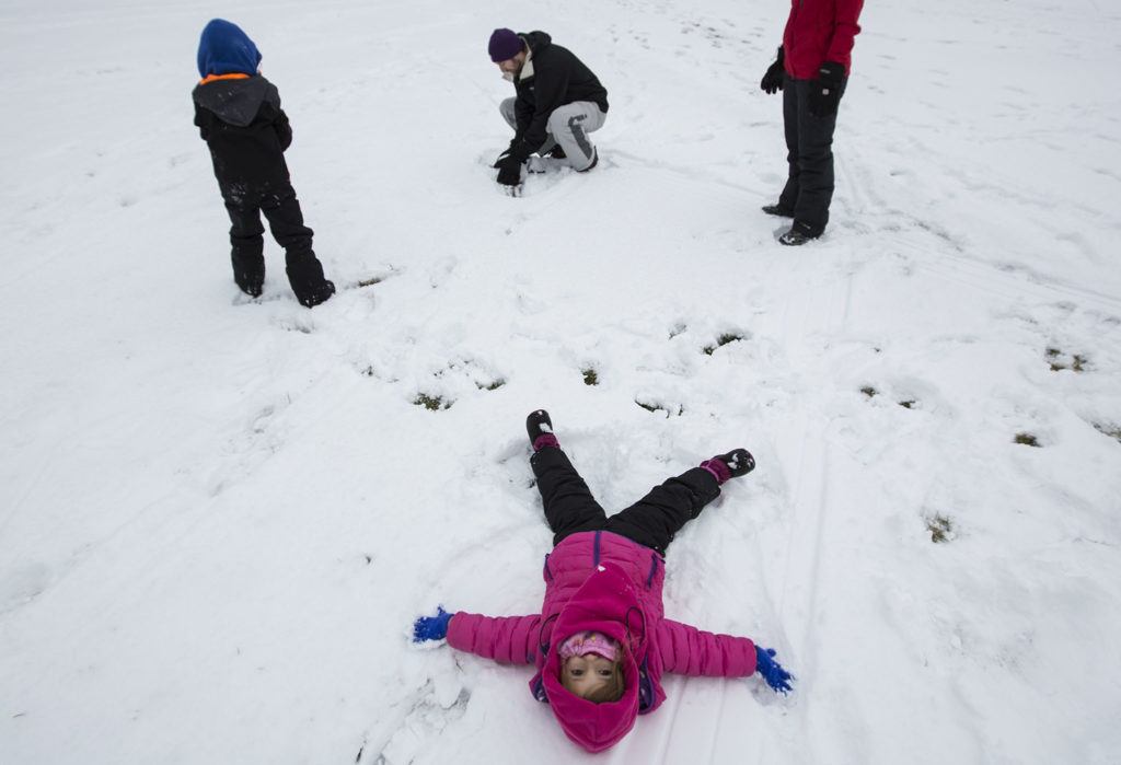 Rada Anderson, 3, makes a snow angel while her brother, Declan Anderson, 5, and parents Chris and Erin Anderson build a snowman at College Place Middle School on Monday in Lynnwood. (Daniella Beccaria / The Herald) 

