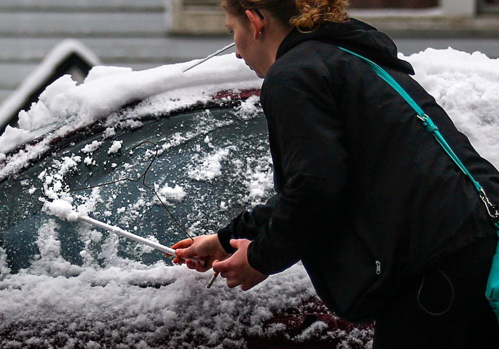 Having tried a piece of cardboard, Hanna Weaver uses a coat hanger to remove snow and ice from her car in north Everett early Monday. (Dan Bates / The Herald)
