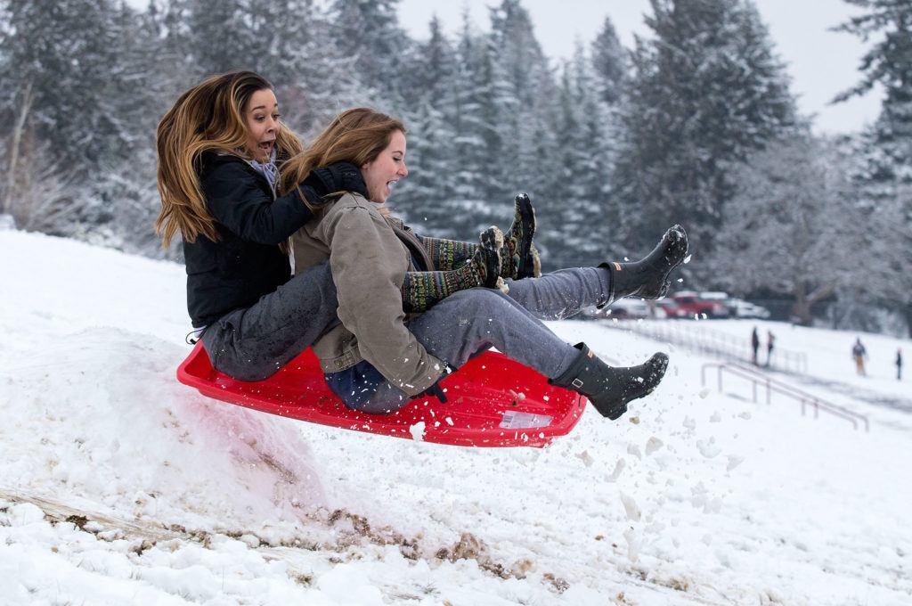 Kaitlyn Nguyen (left) and Grace McCullough scream as they hit a jump while sledding at Stanwood High School on Monday. (Andy Bronson / The Herald) 
