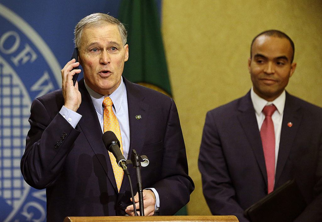 Washington Gov. Jay Inslee briefly speaks into his phone after it rang during a news conference, Thursday, Feb. 23, at the Capitol in Olympia, as general counsel Nick Brown looks on at right. (AP Photo/Ted S. Warren)
