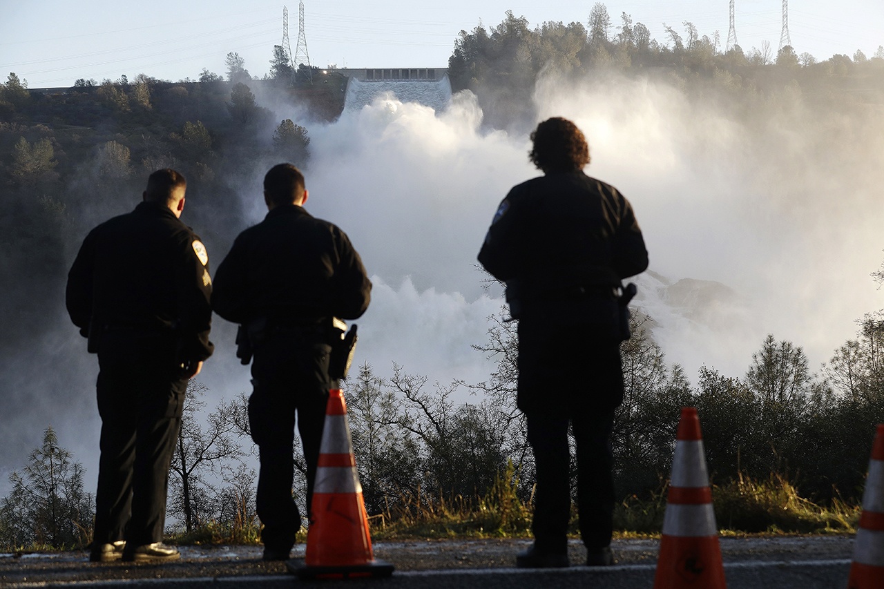 Police officers watch the Oroville Dam’s main spillway from a lookout point Tuesday, Feb. 14, in Oroville, California. Crews working around the clock atop the crippled Oroville Dam have made progress repairing the damaged spillway, state officials said Tuesday. (AP Photo/Marcio Jose Sanchez)