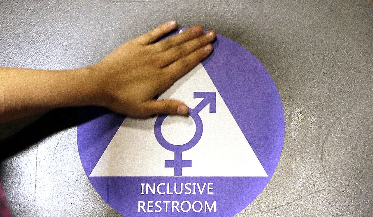 In this 2016 photo, a new sticker is placed on the door at the ceremonial opening of a gender neutral bathroom at Nathan Hale High School in Seattle. A government official says the Trump administration will revoke guidelines that say transgender students should be allowed to use bathrooms and locker rooms matching their chosen gender identity. (AP Photo/Elaine Thompson, File)