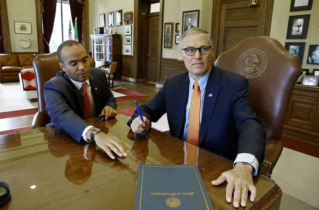 Washington Gov. Jay Inslee looks up after signing an executive order, Thursday, Feb. 23, in his office at the Capitol in Olympia, as general counsel Nick Brown looks on. The order ensures that state workers don’t help carry out President Donald Trump’s immigration policies. (AP Photo/Ted S. Warren)
