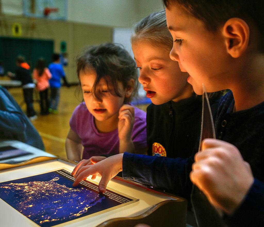 Highland Elementary School first-graders (from left) Cheyenne Hampton, Addison Vaule and Alden Jordan enjoy viewing photographic transparencies taken from space at one of many displays brought into the school Thursday by Pacific Science Center’s Science on Wheels program. (Dan Bates / The Herald)
