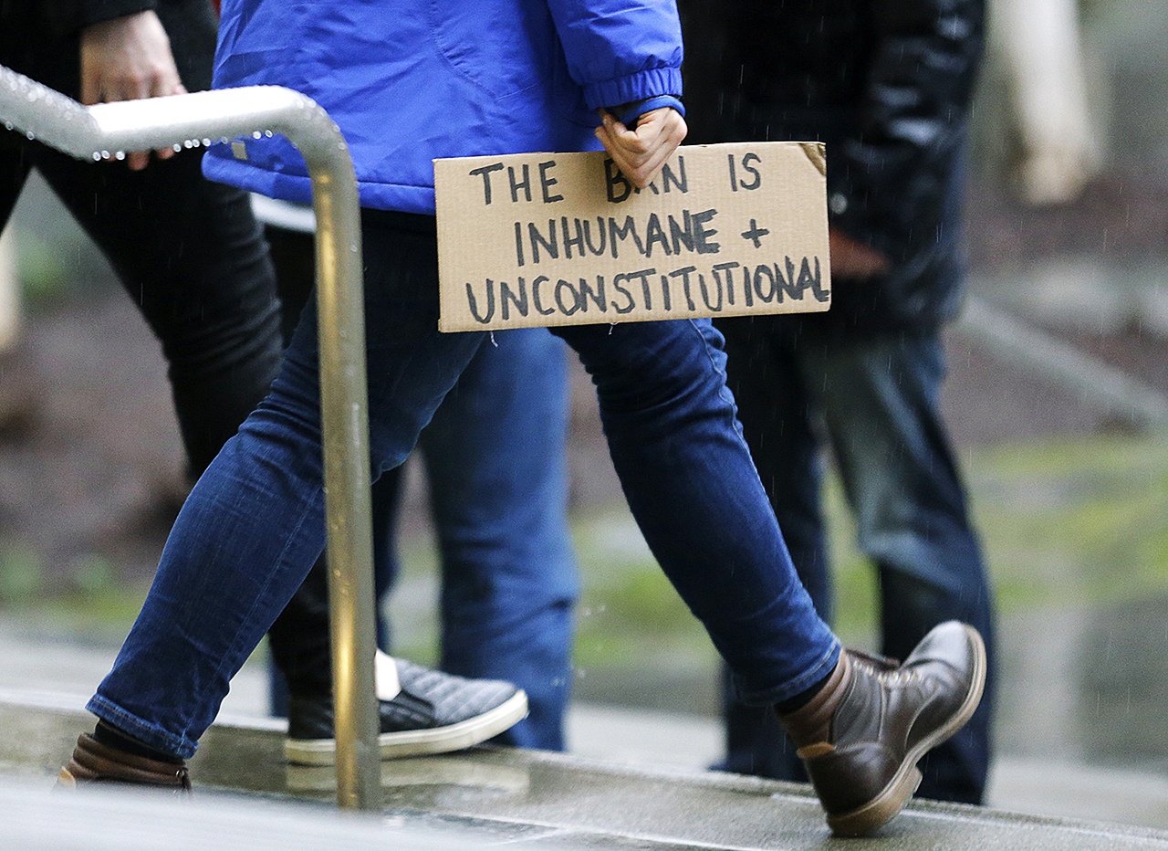 A person walks away from the federal courthouse in Seattle carrying a sign that reads “The Ban is Inhumane and Unconstitutional” on Friday, Feb. 3, following a hearing in federal court in Seattle. (AP Photo/Ted S. Warren)
