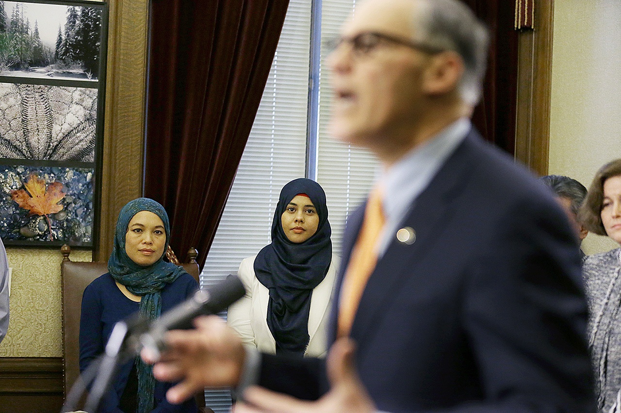 Rokaih Vansot (left), a member of the Washington state chapter of the Council on American-Islamic Relations, stands with Aishah Bomani (center), the principal of Seattle’s Makkah Islamic School, as they listen to Washington Gov. Jay Inslee talk to reporters, Thursday, Feb. 23, at the Capitol in Olympia after Inslee signed an executive order to ensure that state workers don’t help carry out President Donald Trump’s immigration policies. (AP Photo/Ted S. Warren)