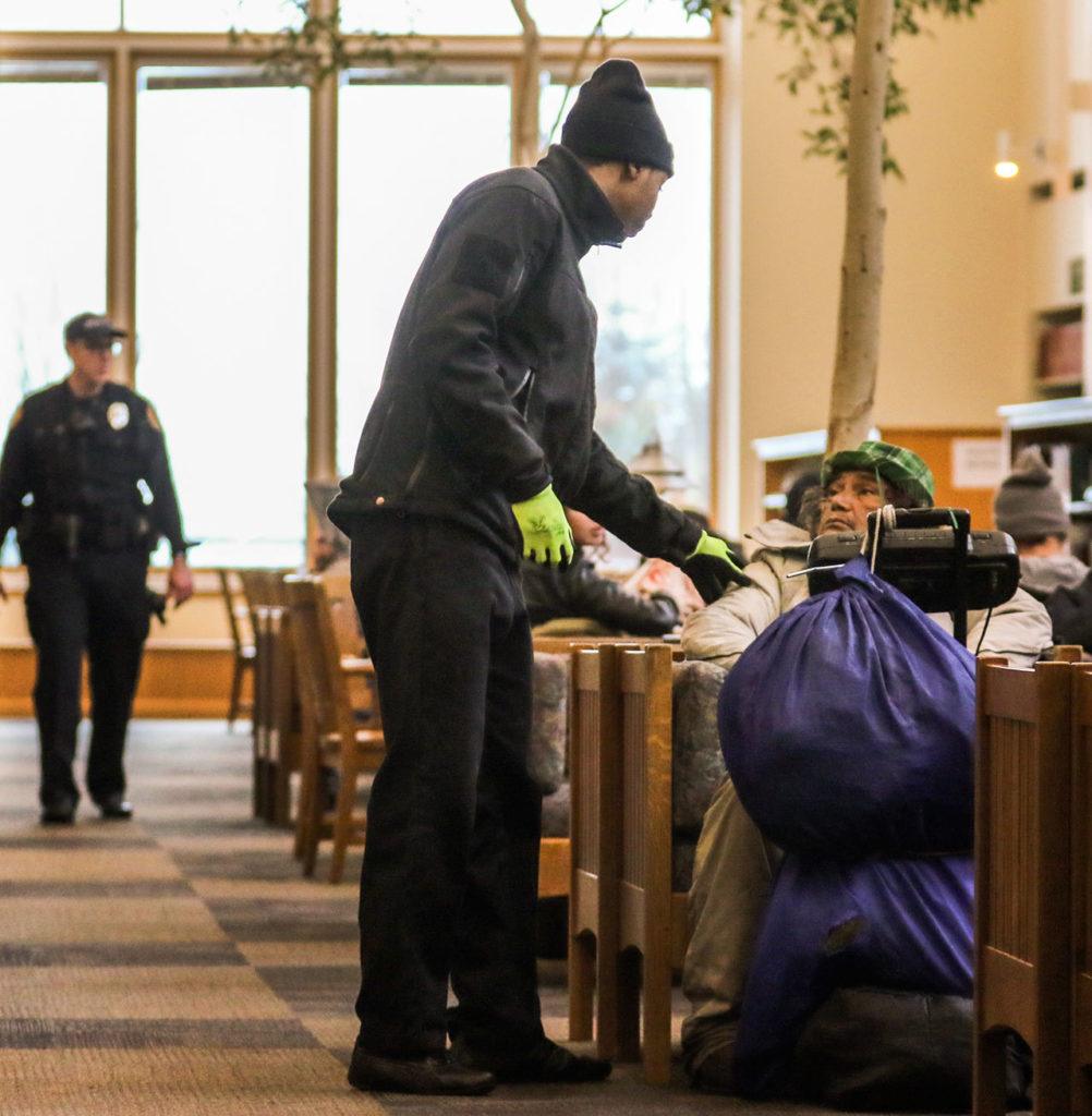 Security guard Rashad Smith wakes a library patron and asks them to leave Wednesday afternoon at the Everett Public Library. (Kevin Clark / The Herald)
