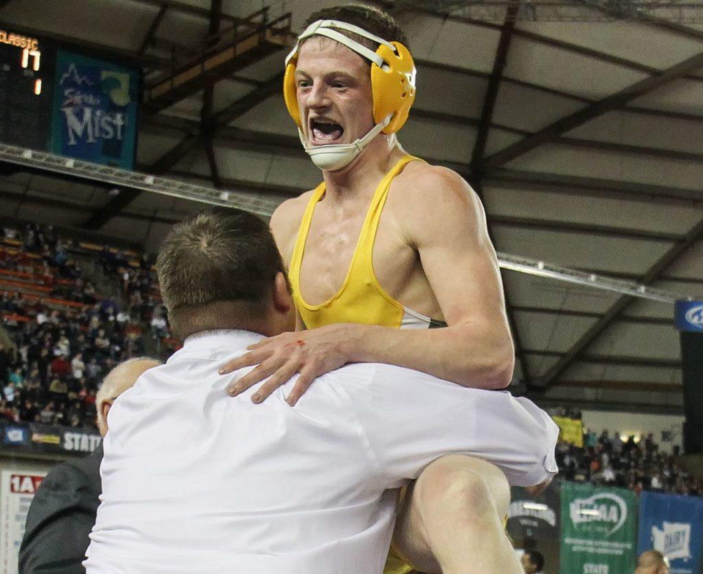 Darrington’s Gage Burtenshaw jumps into the arms of his coach, Andy West, after defeating Wilbur-Creston’s Joe Peasley in the 160-pound class Saturday during Mat Classic XXIX. (Kevin Clark / The Herald)
