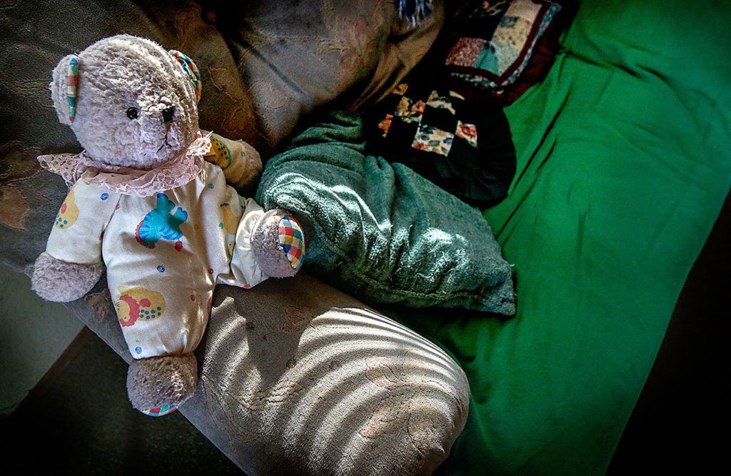 A cuddly stuffed bear in a clown suit sits on the arm of the couch where Gordon “Casey” Powell Jr. slept for five years at his sister’s home in Centralia after she became his legal guardian. The sofa has a permanent trough where her brother slept. (Dan Bates / The Herald)
