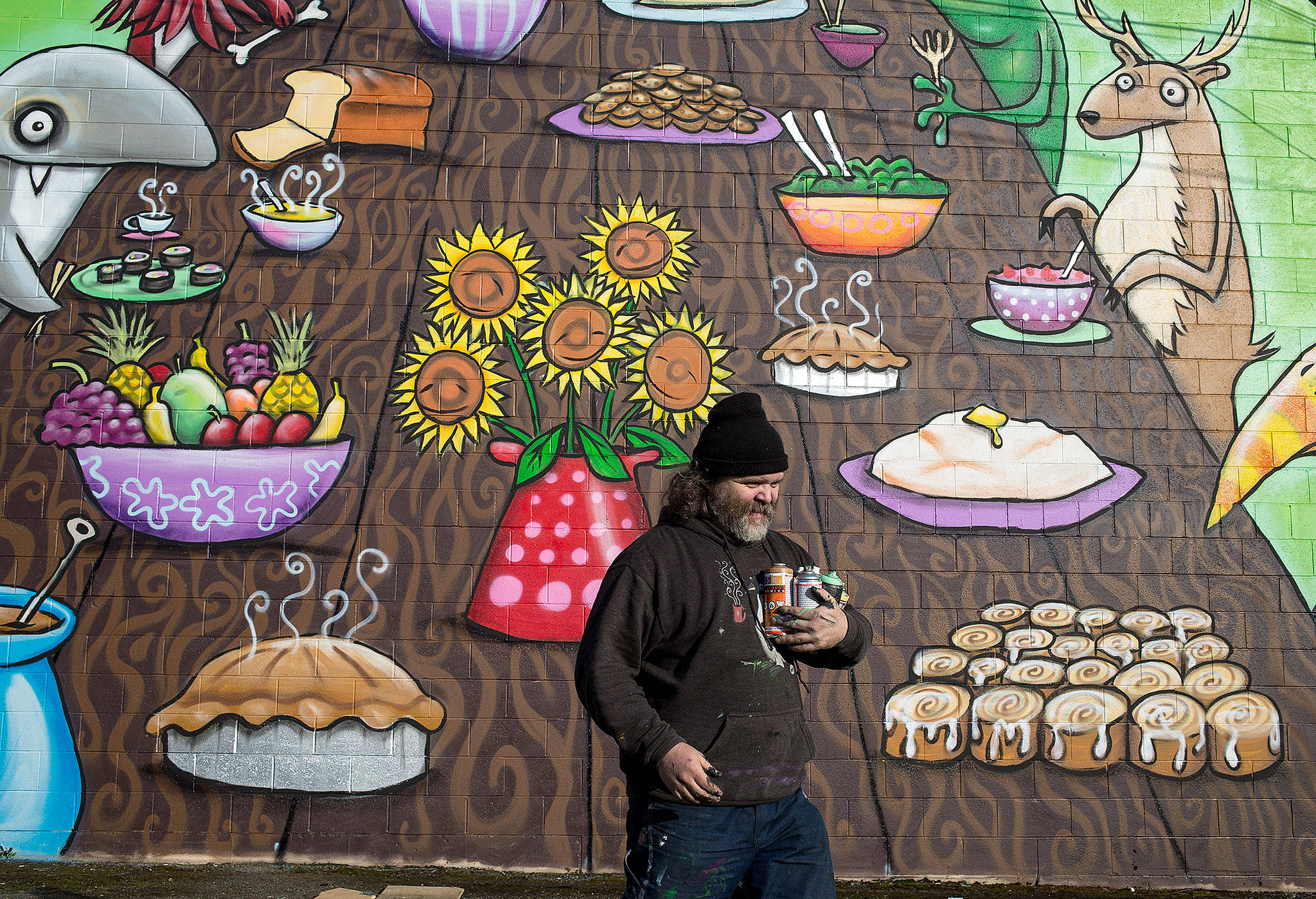 Artist Henry Ward carries his spray paints back to his car after finishing a mural entitled “Table of Diversity” on the west side of the Everett United Church of Christ. The spray paint and acrylic mural took four days to complete. He volunteered his time in support of the Interfaith Association of Western Washington, which runs a family homeless shelter in Everett. (Andy Bronson / The Herald)