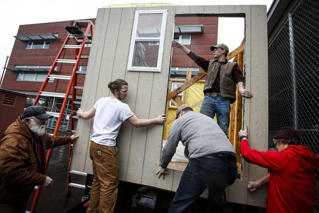 Snohomish High School students Grant Olson (center left) and Bryan Slavin (top) work alongside other students and faculty on Saturday to install a wall on a tiny house being built for a multi-school construction competition. After the contest, the structures will be donated for use as transitional shelters for homeless people in Seattle. (Ian Terry / The Herald)
