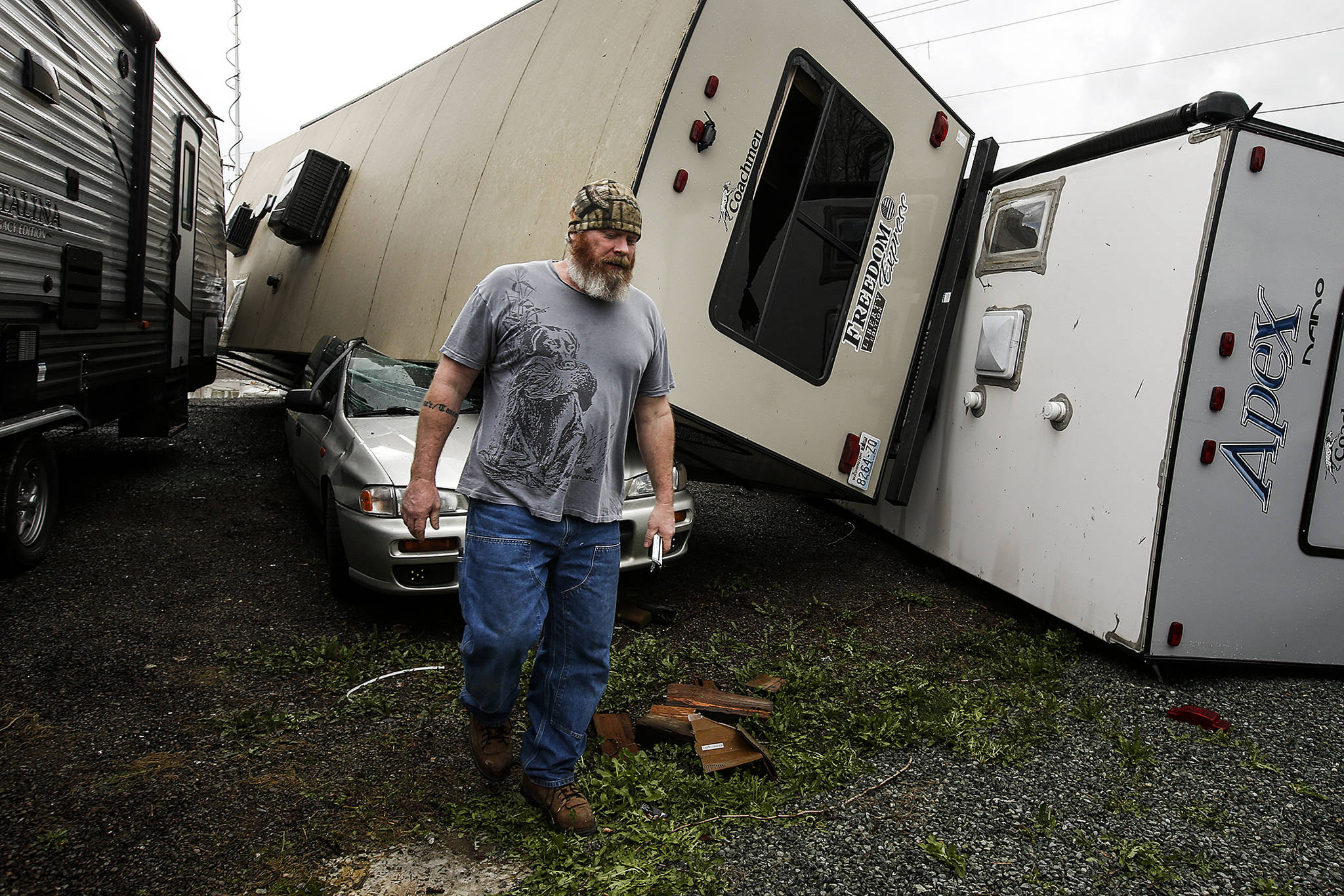 Mark Mills walks near the site of where a tornado damaged trailers and a car at Speedway Chevrolet in Monroe on Thursday morning. Mills lives nextdoor to where the trailers were parked and described hearing a noise that “sounded like a freight train” before coming out to see the overturned campers. (Ian Terry / The Herald)