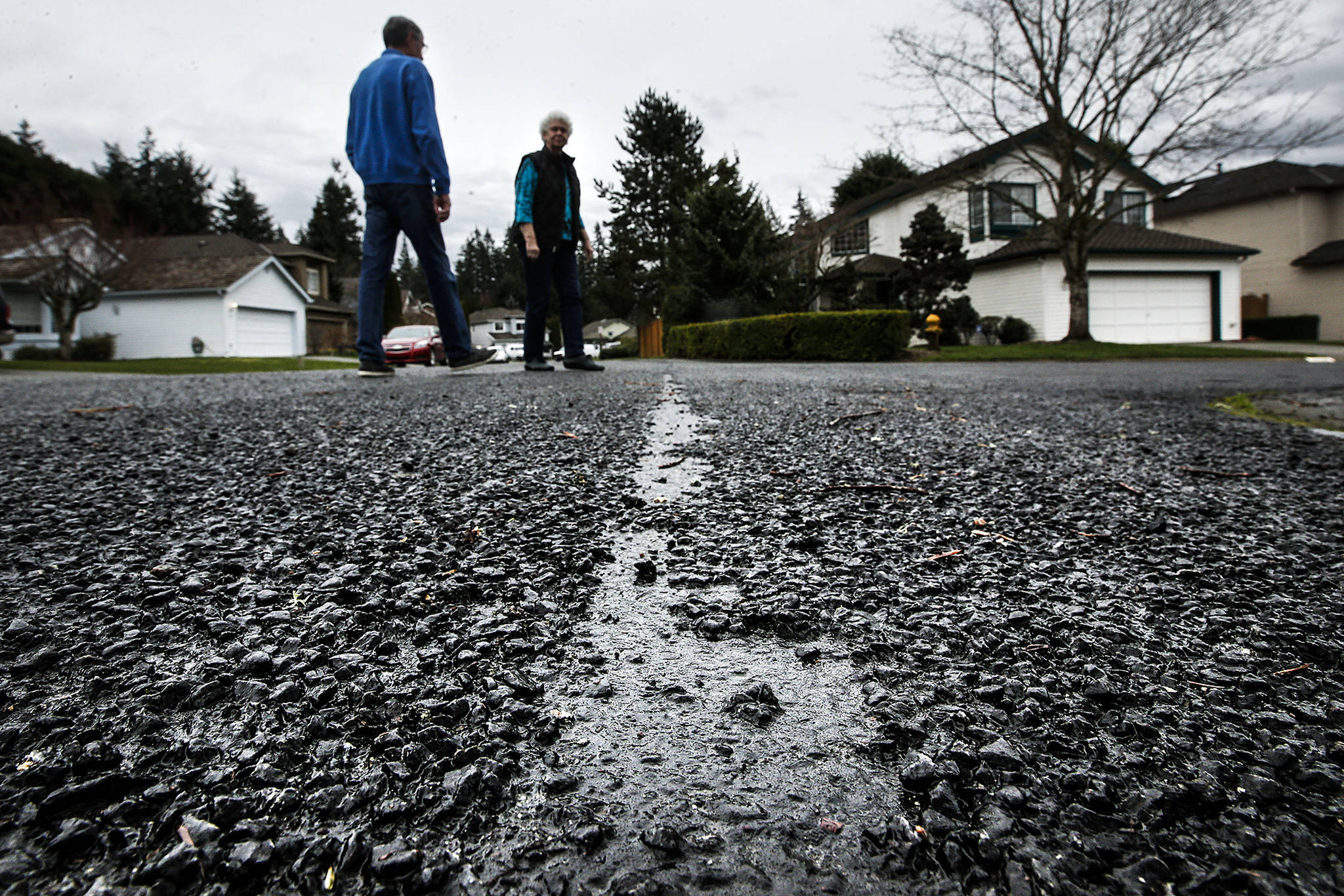 Allen and Bundie Olsen walk near a broken patch of chip seal on Tuesday close to their home in the Wildflower neighborhood of Mill Creek. The rough surface was layed in July and August of 2016 and has since caused problems for residents like the Olsens whose yard and driveway are constantly filled with rocks from the street. (Ian Terry / The Herald)