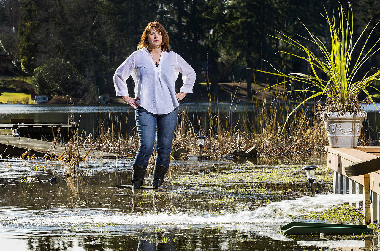 Debbie Bly-Olsen stands in her flooded yard as one of two sump pumps sprays water back into the yard on Lake Serene on Feb. 1 in Lynnwood. (Andy Bronson / Herald file)