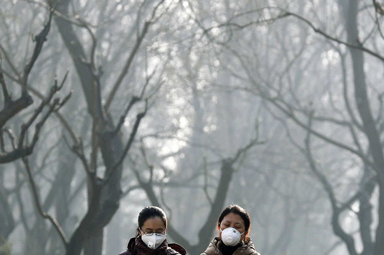 In this Dec. 2016 photo, Chinese women wearing masks to protect themselves from air pollution walk through Ritan Park shrouded by dense smog in Beijing. (AP Photo/Andy Wong, File)