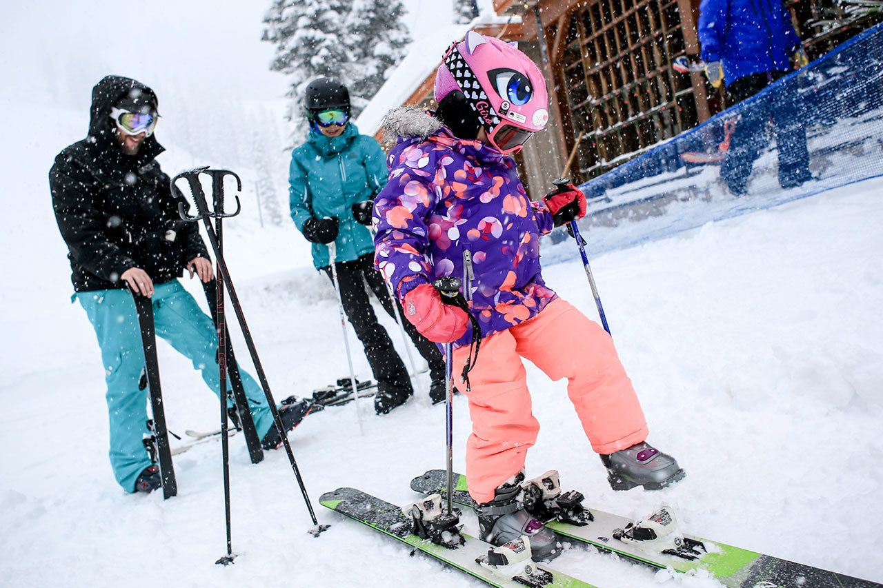 Isabelle Youn tries on her father’s skis with parents Andrew Carlson, left, and Susan Chong looking on Wednesday morning at the Stevens Pass Washington Ski Resort in Skykomish on November 30, 2016. (Kevin Clark / The Herald)