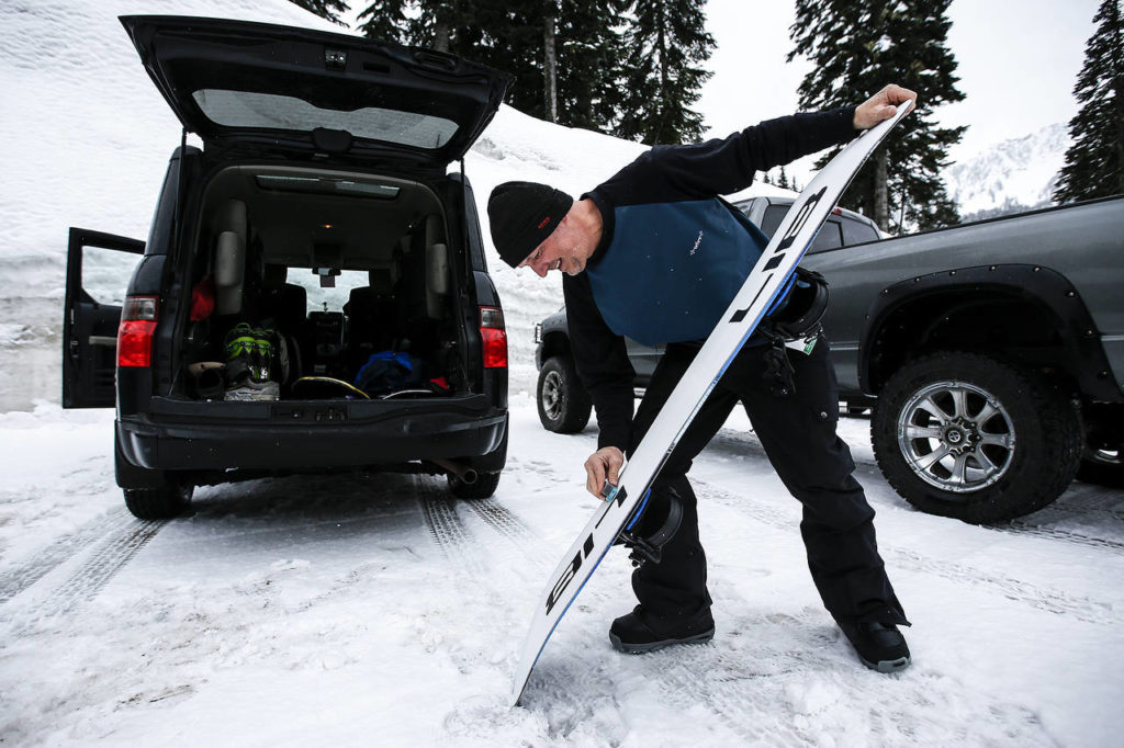 Pete Saari, co-founder of Lib Technologies and Gnu snowboard manufacturers, applies wax to his snowboard before heading out with friend Dave Marx for a few runs at Stevens Pass on Wednesday, March 22. Saari’s company, based in Sequim, focuses on handmade and sustainably built snowboard, ski, surf and skateboard equipment. (Ian Terry / The Herald)
