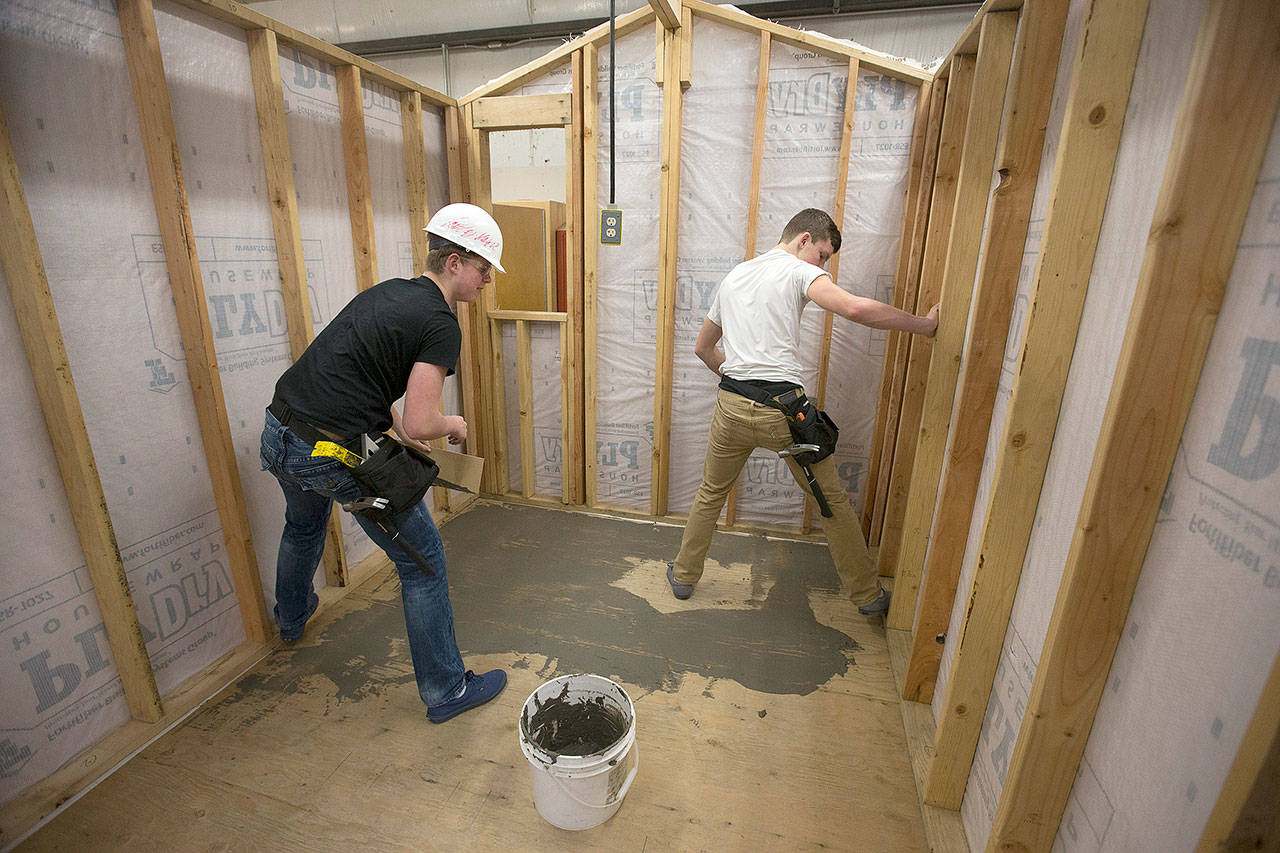 While spreading skim coat, Arlington High sophomore Anthony Whitis almost gets himself stuck in a corner as Caden Smith watches while they work on a tiny home. (Andy Bronson / The Herald)