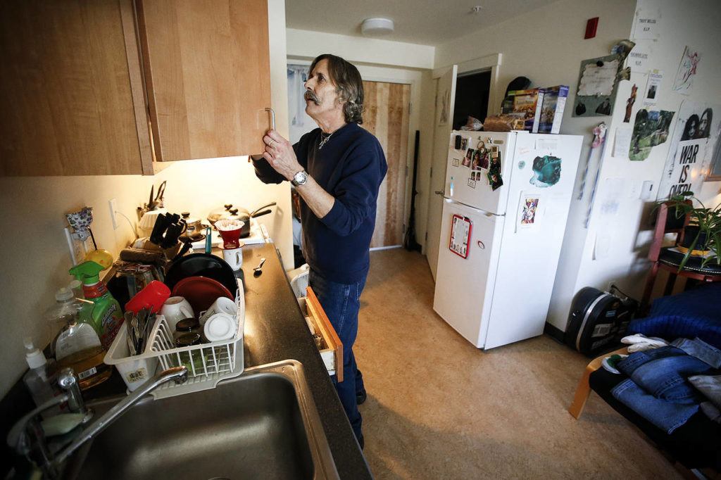 Dennis Bateman, 63, opens a cupboard while making coffee in the kitchen area of his studio apartment at Patrick Place on Aurora Avenue North in Seattle on Wednesday, Feb. 1. Three years ago, Bateman moved into the building addicted to heroin but found that having a safe place to sleep for the first time in his life was crucial to getting sober, which he is now. (Ian Terry / The Herald)
