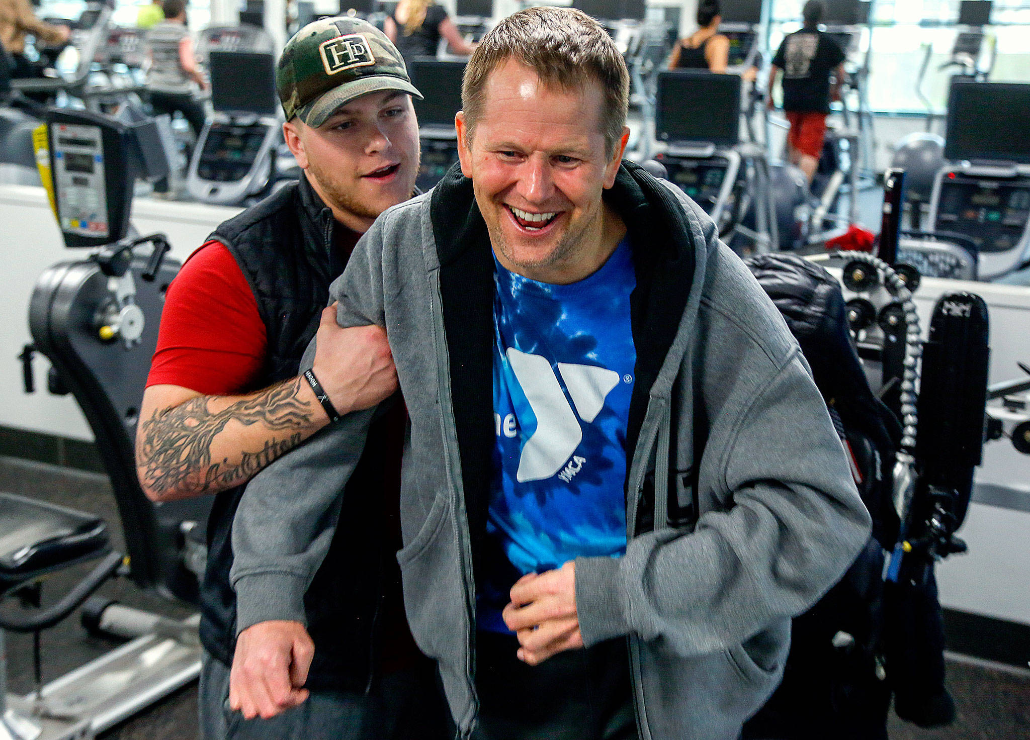 Firmly in the grip of his assistant, Kacey Walker, Stanwood’s Todd Duitsman, who has been paralyzed since a 2014 body surfing accident on Maui, stands up from his wheelchair and attempts a step forward Wednesday at the Marysville YMCA. (Dan Bates / The Herald)