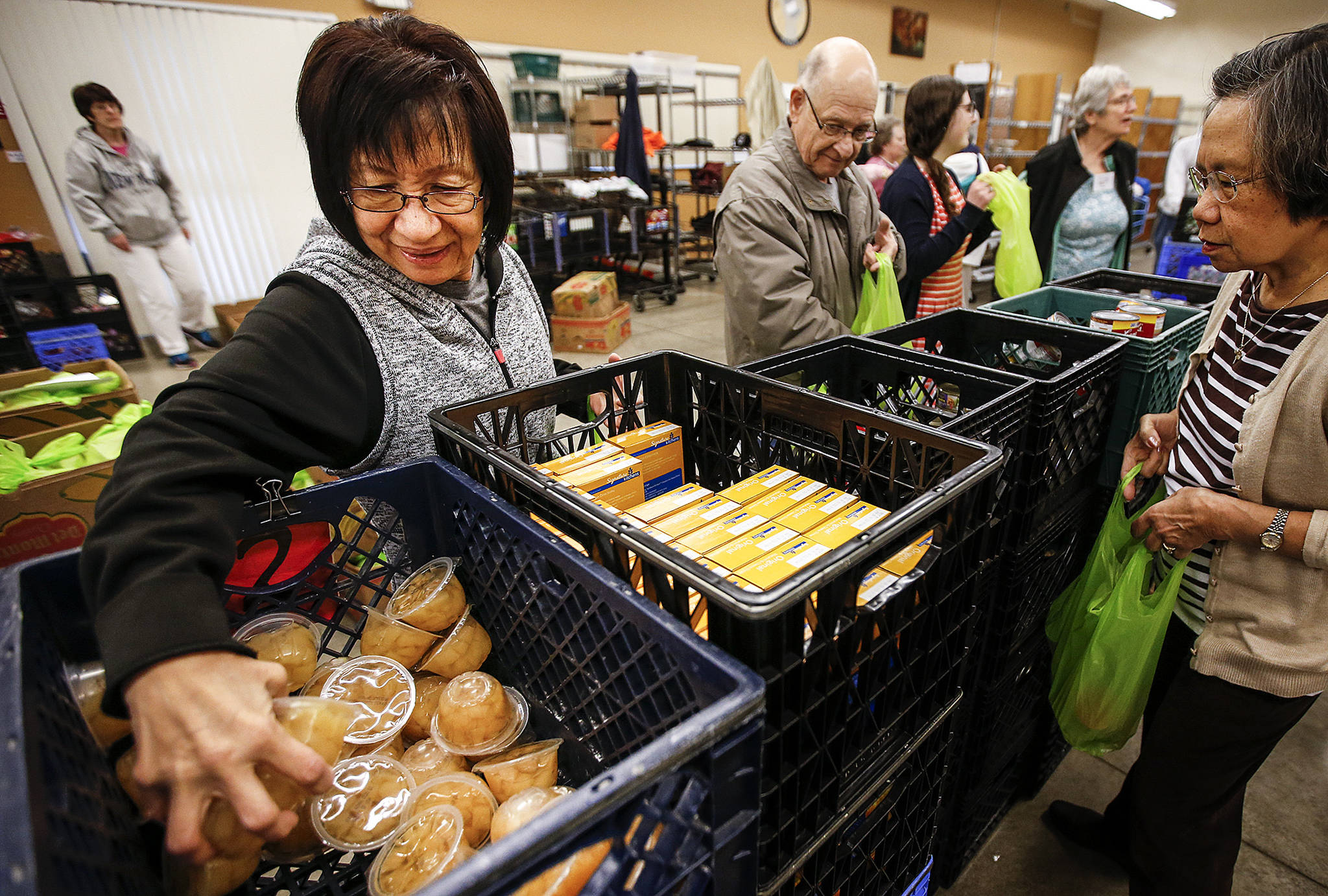 Volunteer Rosalinda Taculad (left), of Marysville, scoops up a handful of fruit containers to be packed into food bags for local schools with kids in need at the Marysville Community Food Bank on April 27. Funding for some of the food bank’s programs comes from Community Development Block Grants which the Trump administration proposes to eliminate. (Ian Terry / The Herald)