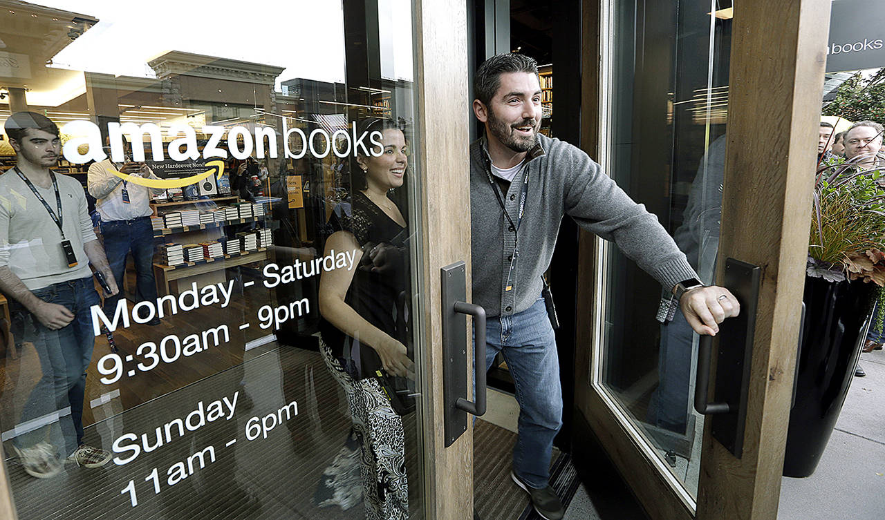 In this 2015 photo, employees smile as they unlock and open the door to the first customers at the opening day for Amazon Books in Seattle, the first brick-and-mortar retail store for online retail giant Amazon. (AP Photo/Elaine Thompson, File)