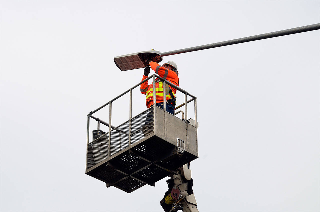 A Washington State Department of Transportation crew member swaps out an old luminaire (in bucket) with a new LED fixture in 2013 near Olympia. Similar upgrades were recently made along Snohomish County highways as part of a $4.6 million lighting project aimed at trimming utility bills. (WSDOT photo)