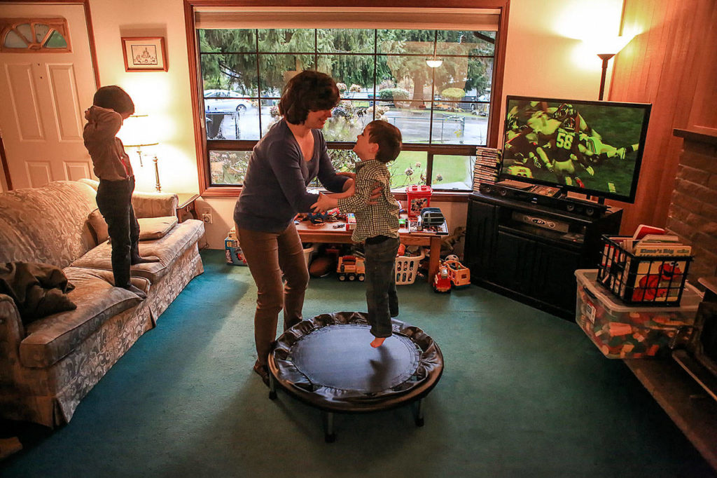 Ian Fisher watches a game as his mother, Deanna Fisher, plays with her youngest son, 4-year-old Colin, who lives with autism, at their home in Bothell. The Fishers plan to donate baby teeth from their youngest sons for a national study that will try to determine if prenatal and early-life exposure to chemicals increases a child’s chances of developing autism. (Kevin Clark / The Herald)
