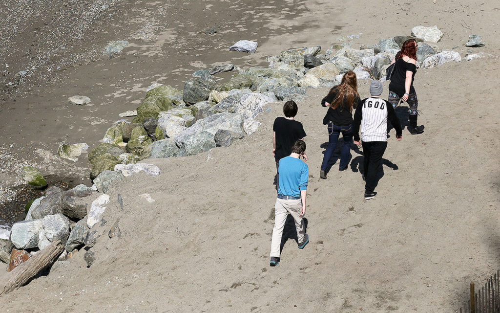 Beachgoers to Howarth Park walk by a rock bulwarks on Tuesday in Everett. (Andy Bronson / The Herald)
