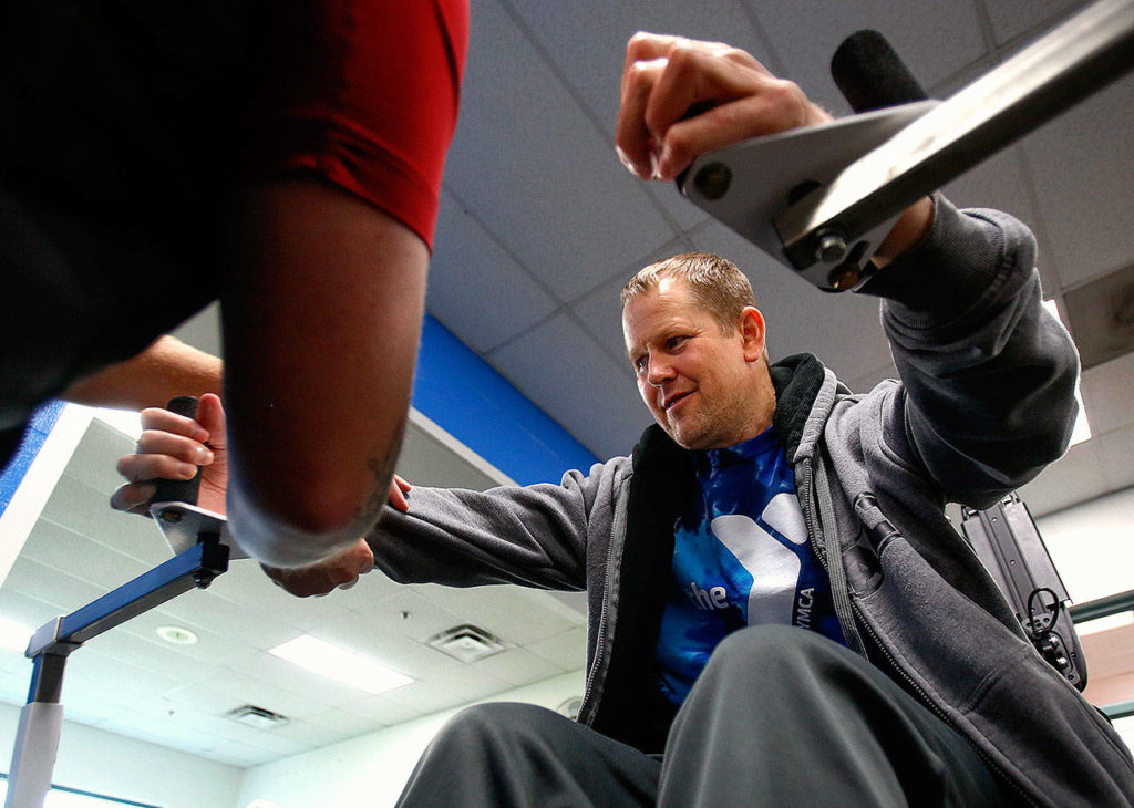 Walker helps Duitsman position himself in a custom Uppertone exercise apparatus. (Dan Bates / The Herald)
