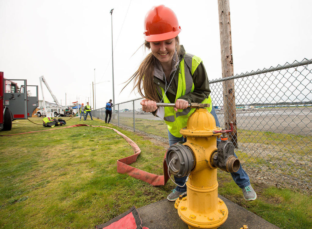 Natalie Giard leans hard as she opens a fire hydrant as she and other teens learn what it take to be a firefighter at the Trade UP event at Arlington Airport on Tuesday. (Andy Bronson / The Herald)
