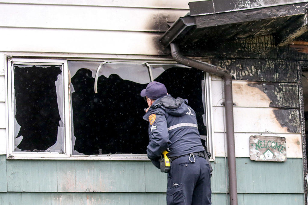 An Everett police officer examines the remains of a house fire Saturday morning in Everett. (Kevin Clark / The Herald)
