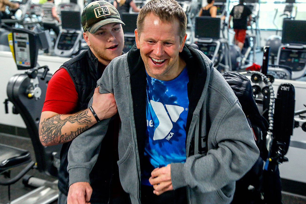 Firmly in the grip of his assistant, Kacey Walker, Stanwood’s Todd Duitsman, who has been paralyzed since a 2014 body surfing accident on Maui, stands up from his wheelchair and attempts a step forward Wednesday at the Marysville YMCA. (Dan Bates / The Herald)